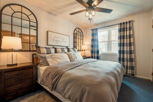 Cozy bedroom with a large bed, decorative mirrors, and plaid curtains, featuring warm lighting and a ceiling fan.