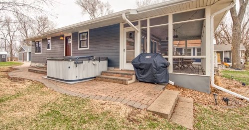 A cozy home exterior with a screened porch, hot tub, and patio area surrounded by trees and grass.