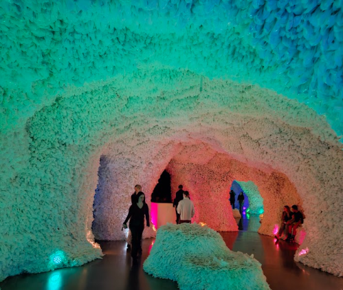 A colorful, cave-like installation made of textured white materials, with visitors exploring the illuminated space.