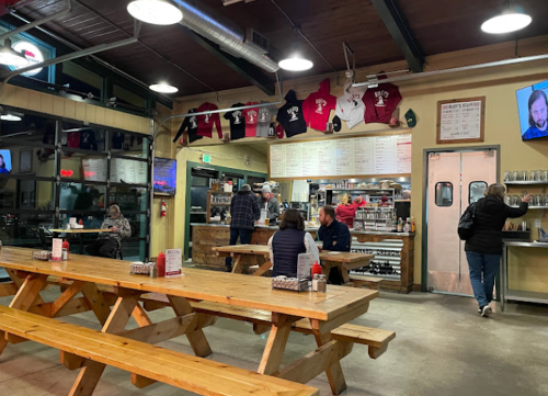 Interior of a casual dining restaurant with wooden tables, patrons eating, and a menu board on the wall.