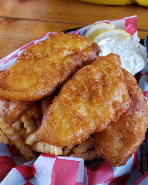 A plate of golden-brown fried fish fillets served with lemon wedges and a side of dipping sauce.