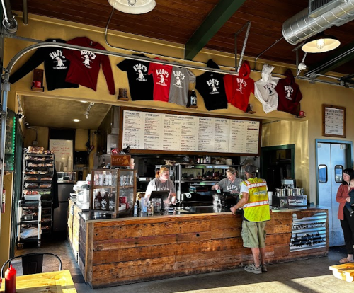 A cozy café with a wooden counter, staff serving drinks, and T-shirts displayed on the wall.