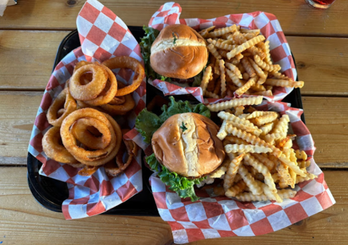 A tray with two burgers on lettuce, crinkle-cut fries, and onion rings, all served in red and white checkered paper.