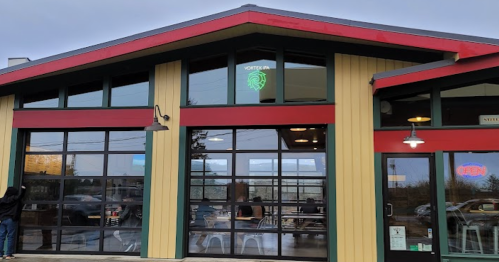 Exterior of a modern restaurant with large glass doors, a green sign, and a "OPEN" sign, set against a cloudy sky.