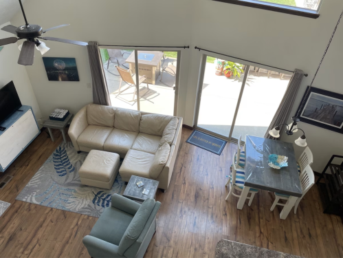 A spacious living room with a beige sectional sofa, dining area, and large windows overlooking a patio.