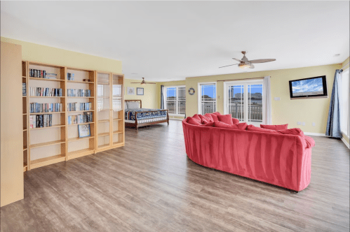 Spacious living area with a pink couch, bookshelf, and large windows offering scenic views.