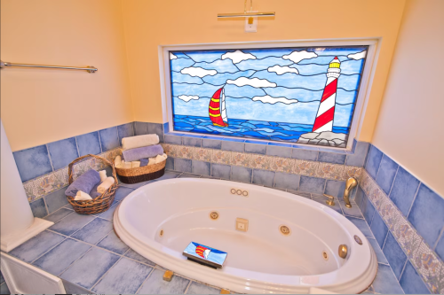 A cozy bathroom featuring a jetted tub, blue tiled walls, and a colorful stained glass window with a lighthouse and sailboat.