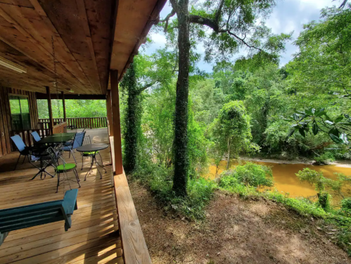 A wooden porch overlooks a lush green landscape and a winding river, surrounded by trees and natural beauty.