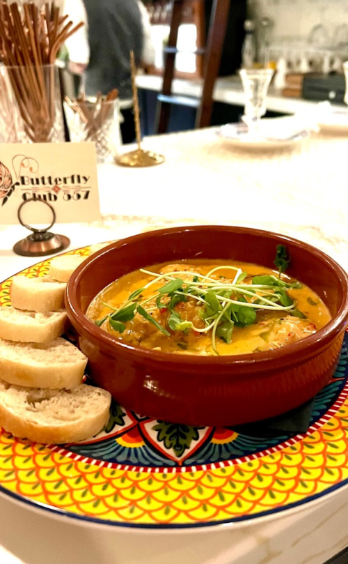 A vibrant dish in a bowl with sauce and herbs, served with slices of bread on a colorful patterned plate.