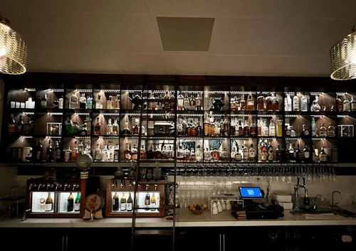 A well-lit bar shelf filled with various bottles of liquor and glassware, featuring a modern design.