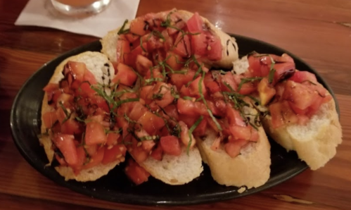 A plate of bruschetta topped with diced tomatoes and fresh basil on toasted bread.