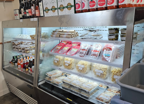 A refrigerated display case filled with various packaged foods, including pasta, sauces, and drinks.