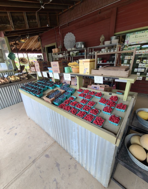 A market stand displaying colorful baskets of blueberries and raspberries, with price signs and rustic decor.