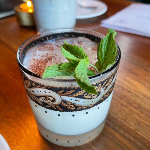 A decorative glass filled with a creamy drink, ice, and topped with fresh mint leaves.