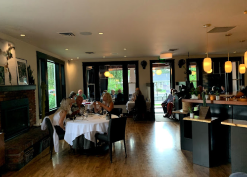 A cozy restaurant interior with diners at tables, soft lighting, and a fireplace, creating an inviting atmosphere.