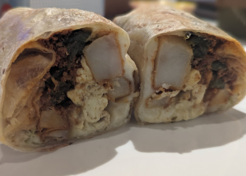 Close-up of a cut burrito, revealing layers of potatoes, eggs, and spices inside a soft tortilla.