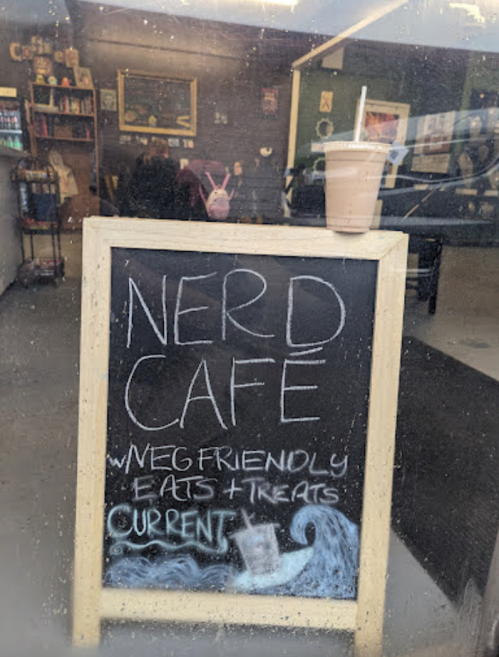 A chalkboard sign outside a café reads "NERD CAFE" with details about vegan-friendly eats and treats.