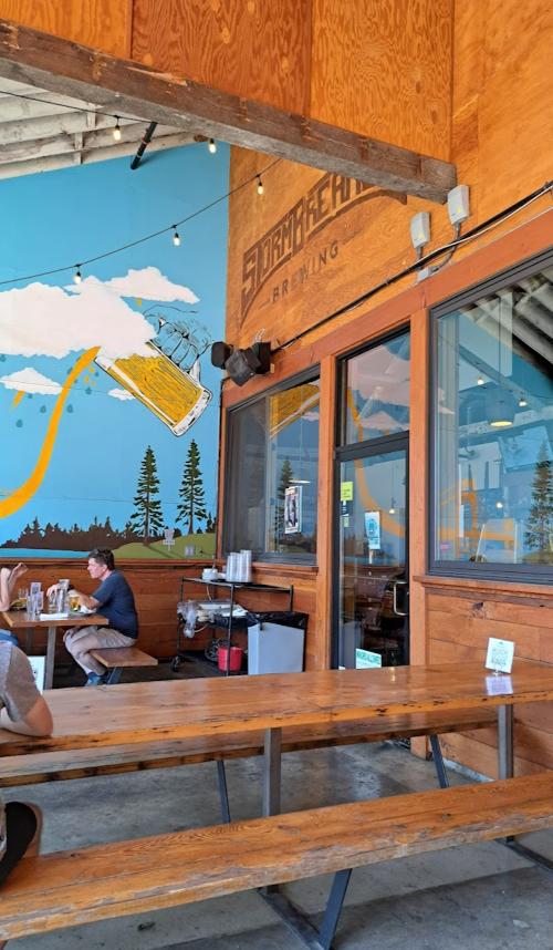 Interior of a brewery with wooden tables, a mural of a beer can, and patrons enjoying their meals.