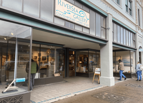 Exterior of RiverSea Gallery, showcasing contemporary art, with an "Open" sign and people walking by.