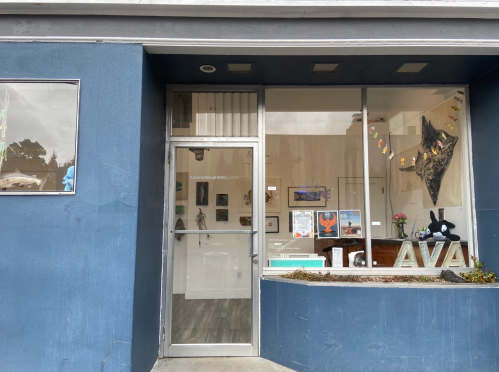 Exterior view of a gallery with a glass door, showcasing art and decorations in the window.