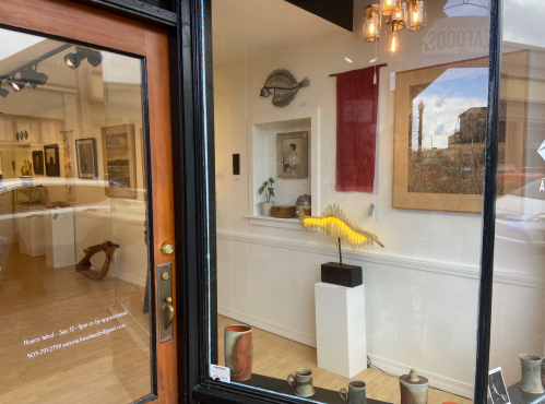 A gallery window displaying art pieces, including a yellow sculpture, framed artwork, and decorative items.