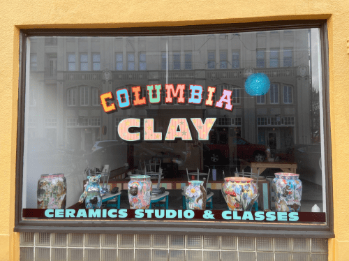 Window display of "Columbia Clay" featuring colorful ceramic pots and a blue hanging light.