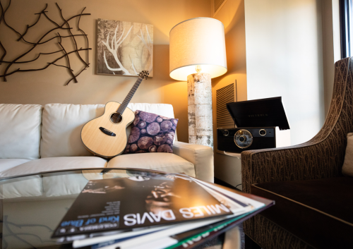 A cozy living room with a guitar, decorative pillow, lamp, and a vintage record player on a glass table.