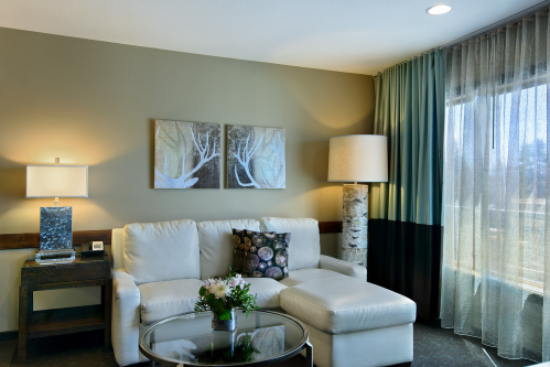 A cozy living area featuring a white sofa, decorative pillows, a glass table, and large windows with sheer curtains.