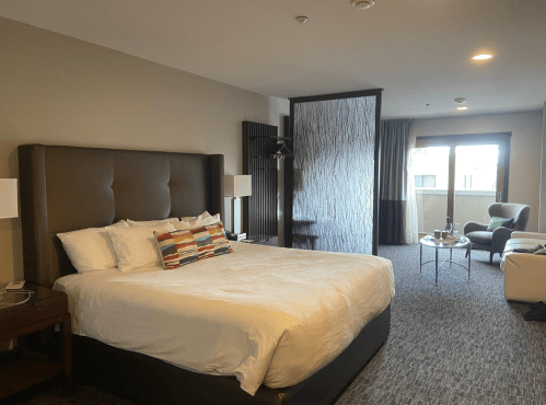 A modern hotel room featuring a king-sized bed, seating area, and large windows with natural light.
