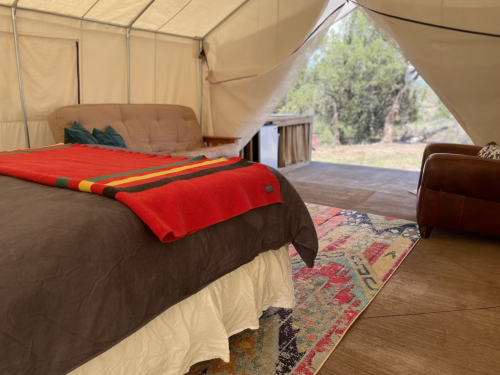 Cozy glamping tent interior with a bed, colorful blanket, and a view of nature through the open entrance.