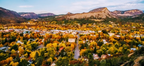 Aerial view of a colorful autumn landscape with mountains and a small town surrounded by trees.