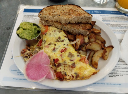 A plate with an omelette, roasted potatoes, toast, and a side of guacamole and radish.