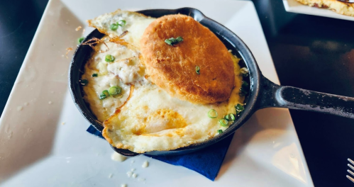 A cast iron skillet with baked eggs, cheese, and a golden biscuit, garnished with green onions on a white plate.