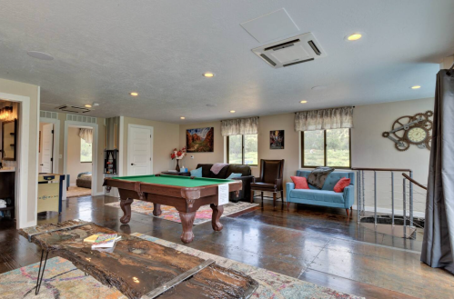 A spacious room with a pool table, seating area, and large windows overlooking greenery. Cozy and inviting atmosphere.