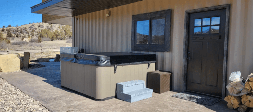 A hot tub beside a modern building entrance, with steps leading up and a small storage bin nearby.