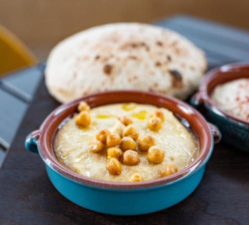 A bowl of creamy chickpea dish topped with chickpeas, served with flatbread on a wooden table.