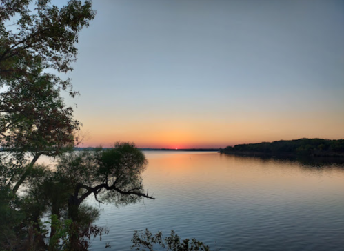 A serene sunset over a calm lake, with trees framing the view and soft colors reflecting on the water.