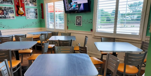 A bright restaurant interior with empty tables, music-themed decor, and a TV on the wall.