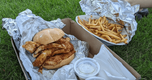 A sandwich with fried fish fillets on a bed of foil, accompanied by a side of fries in a cardboard container.