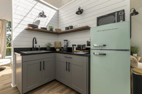 Modern kitchen with gray cabinets, black countertops, a mint green fridge, and various appliances in a bright, airy space.