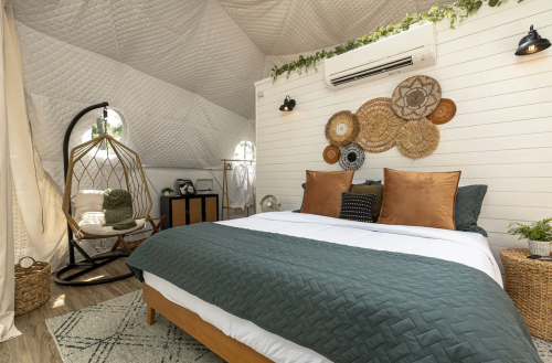 Cozy bedroom with a green quilt, decorative wall hangings, a hanging chair, and natural light from arched windows.