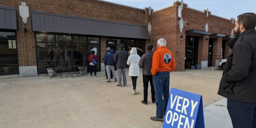 A line of people waiting outside a store with a "VERY OPEN" sign in front.