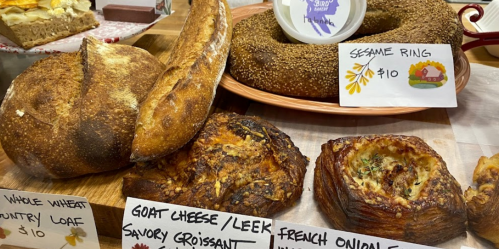 A display of various baked goods, including a sesame ring, savory croissant, and French onion pastry, with price tags.