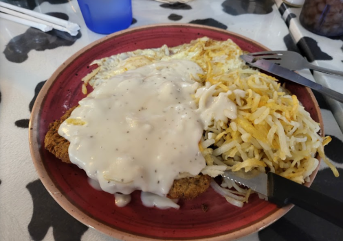 A plate of chicken fried steak topped with white gravy, served with hash browns and a side of eggs.