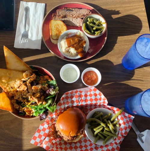 A table with a plate of brisket, mashed potatoes, green beans, a salad, and a fried chicken sandwich.