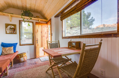 Cozy interior of a tiny home with a wooden table, chairs, and large windows showcasing a natural landscape outside.