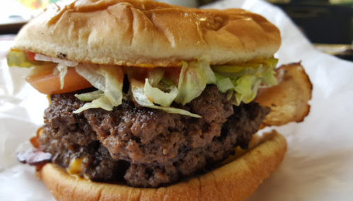 A close-up of a juicy hamburger with lettuce, tomato, pickles, and ketchup on a soft bun.