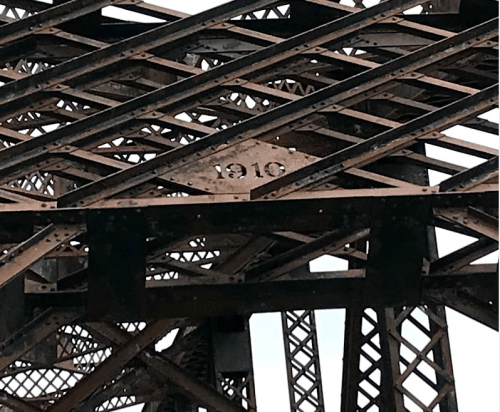 Close-up of a metal bridge structure with the year "1910" engraved on it, showcasing intricate ironwork.
