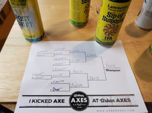 A tournament bracket on paper with names and a champion title, surrounded by cans of beer on a wooden table.