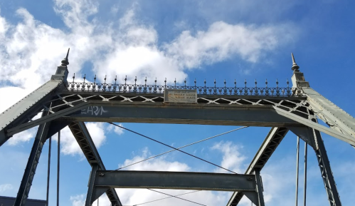 A historic metal bridge with decorative spires against a blue sky with clouds.